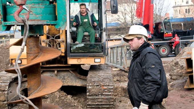 Ein Bauarbeiter begutachtet eine große Bohrschraube, im Hintergrund ein Mann im Baufahrzeug (öffnet Vergrößerung des Bildes)