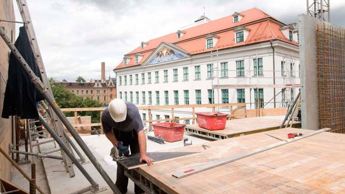 A construction worker cuts a board on the shell, a white building in the background (opens enlarged image)