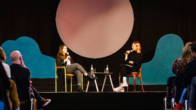 Auf einer Bühne sitzen zwei junge Frauen und diskutieren. Im Hintergrund ist eine Kulisse aus Mond und Wolken (öffnet Vergrößerung des Bildes)