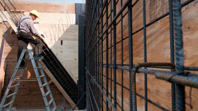 Sich im Bau befindende Gebäudewand, im Hintergrund Bauarbeiter auf einer Leiter (öffnet Vergrößerung des Bildes)