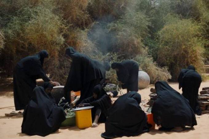 Frauen in schwarzen Hidschabs bereiten draußen ein Feuer vor