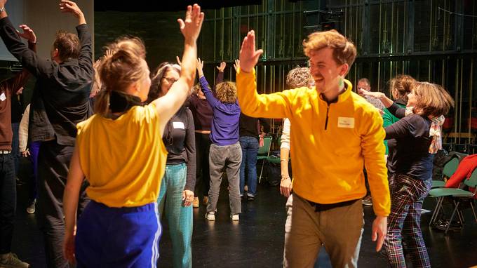 Teilnehmende der Gastspielwerkstatt bei einem Tanzworkshop auf einer Theaterbühne, im Vordergrund geben sich zwei Personen ein High-Five. (öffnet Vergrößerung des Bildes)