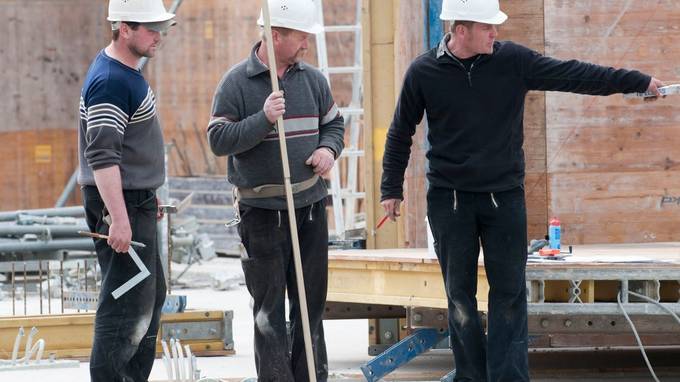 Three construction workers talking, one pointing to the right (opens enlarged image)