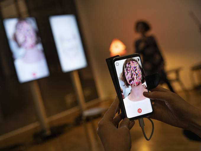 Zwei Hände umfassen ein Handy, auf dessen Bildschirm eine Frau mit unkenntlichem Gesicht