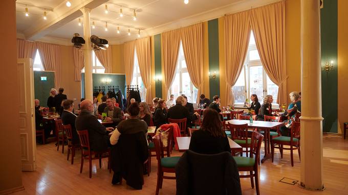 Foyer-Saal des Metropol in Bernburg, wo zahlreiche Teilnehmende der Gastspielwerkstatten sich an Tischen sitzend unterhalten. (öffnet Vergrößerung des Bildes)