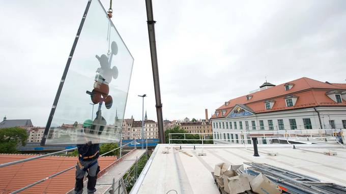 A large pane of glass attached to a crane is held by a construction worker  (opens enlarged image)