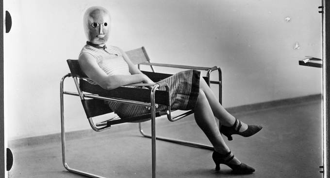 Person im Kleid mit Maske über dem Kopf in einem Sessel