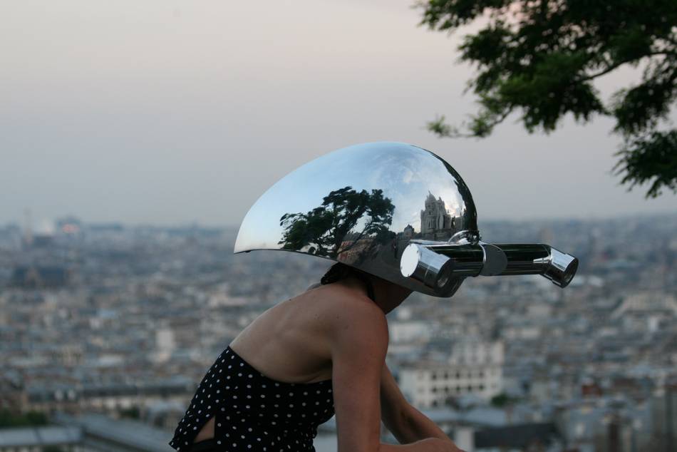 Frau mit einem silbernen Helm mit Röhrenaugen fährt auf Fahrrad durch Paris.