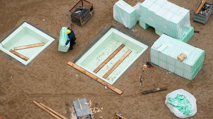 Vogelperspektive auf einen Bauarbeiter, der mit von Planen bedeckten Holzpaletten beschäftigt ist (öffnet Vergrößerung des Bildes)