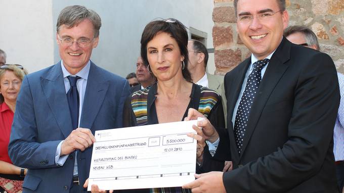 Two men and a woman together hold a large cheque in their hands (opens enlarged image)