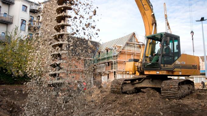 A construction vehicle pulls a large drill out of the ground, mud splashing (opens enlarged image)