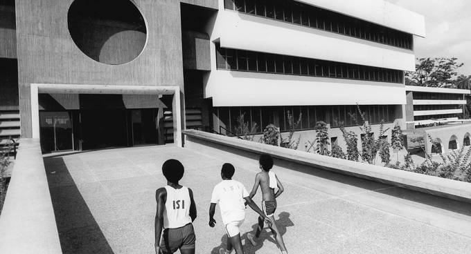 Schwarzweißfoto von drei Kindern in Sportkleidung, die auf ein Gebäude zugehen