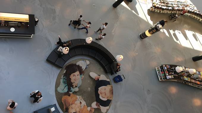 Vogelperspektive auf Saal mit rundem Teppich, darauf drei hochblickende Personen (öffnet Vergrößerung des Bildes)