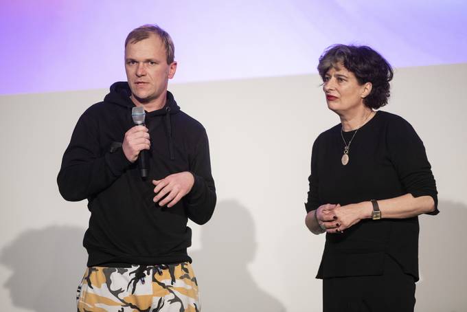 zwei stehende Personen: links Mann mit Mikrofon in der Hand, rechts Frau