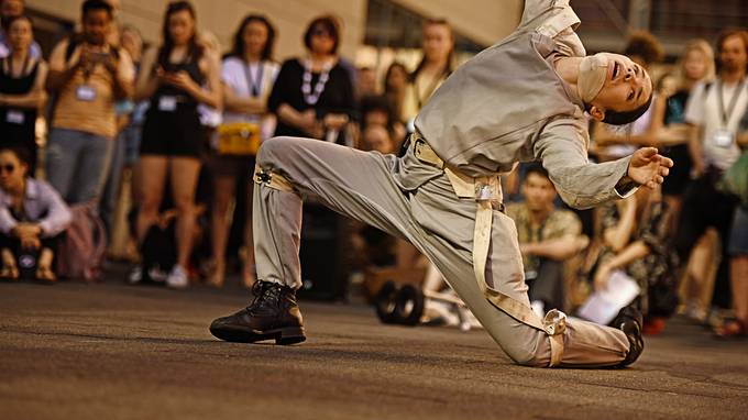Tänzerin in beigem Kostüm tanzt auf der Straße vor einer Gruppe Menschen (öffnet Vergrößerung des Bildes)