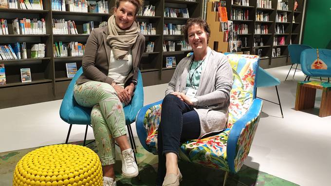 Zwei Frauen in Sesseln lächeln in die Kamera, im Hintergrund Bücherregale (öffnet Vergrößerung des Bildes)